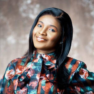 Afua smiles confidently in a colorful floral blouse, posing against a softly blurred studio background.